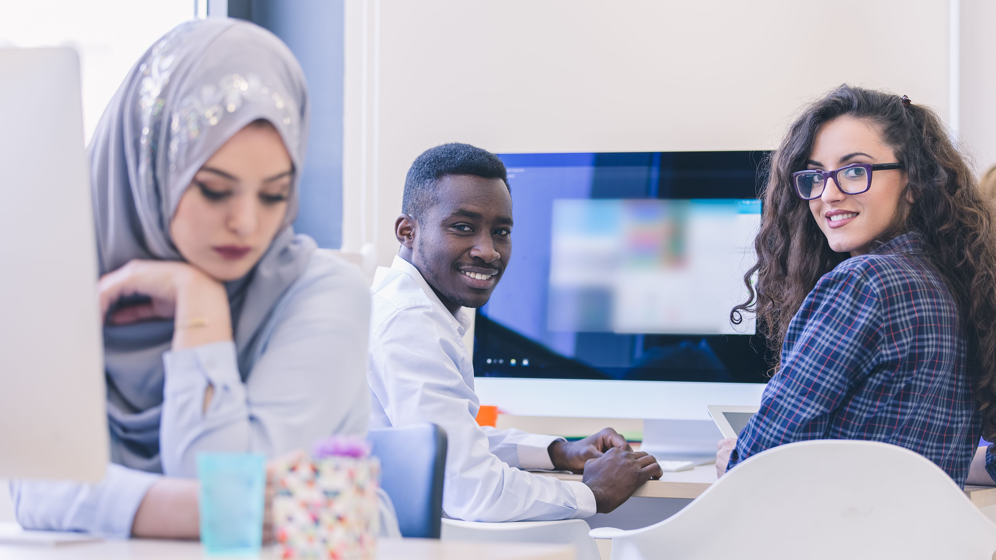 Femme musulmane, homme noir et femme blanche devant leur ordinateur.